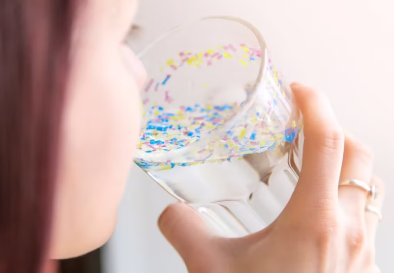 Person som dricker vatten ur ett glas fyllt med färgade mikroplastpartiklar.